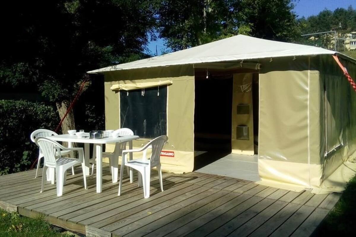 Une tente avec une table et des chaises à l’extérieur, entourée de verdure.