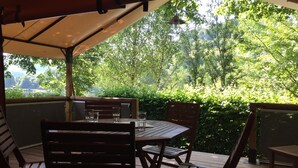 An outdoor patio with a wooden table and chairs, surrounded by lush greenery and trees. - Camping de Matour (Matour)
