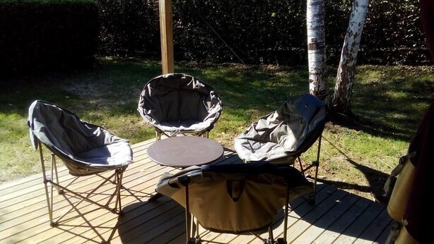 A deck with two chairs and a table, surrounded by a wooden deck and a grassy area with trees. - Camping de Matour (Matour)
