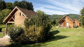 Two wooden cabins with pitched roofs, surrounded by greenery and hills. - Camping de Matour (Matour)