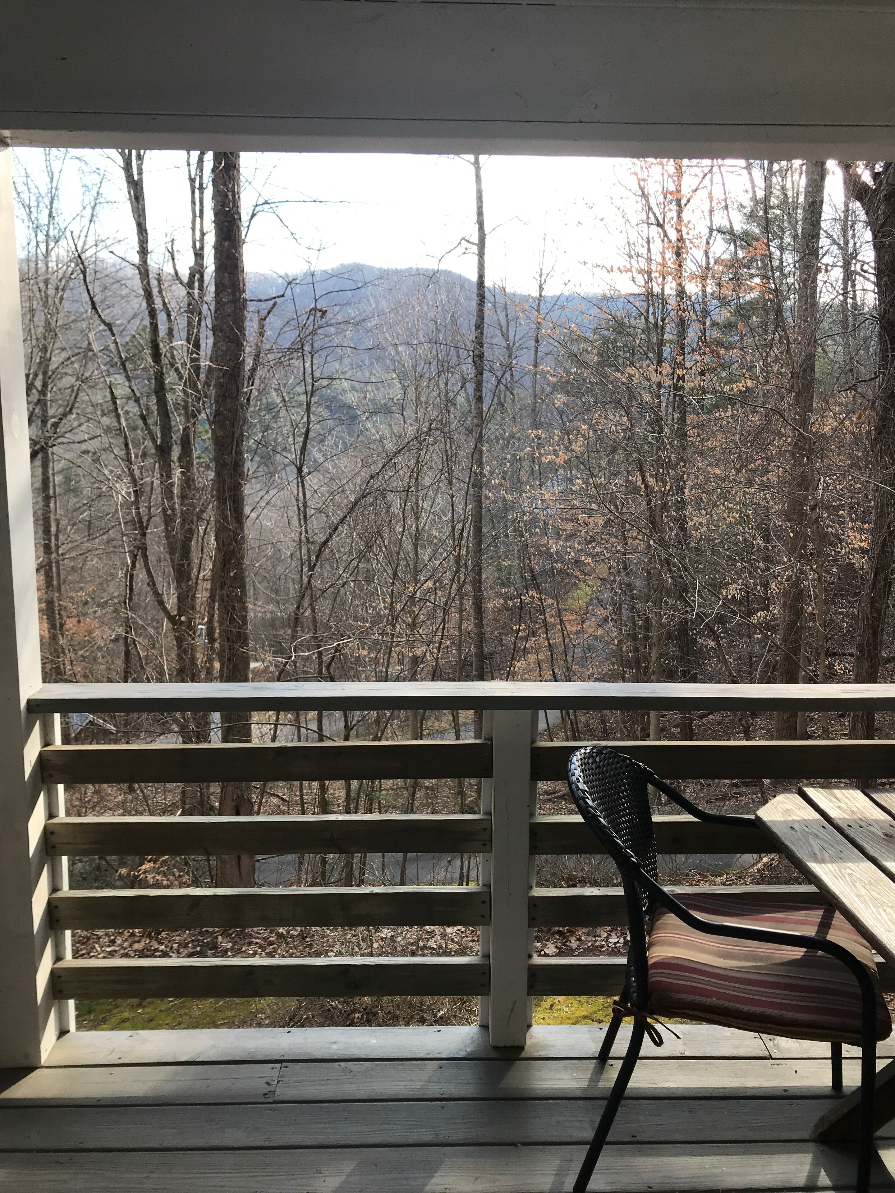 A wooden deck with a bench and a view of a forested area with mountains in the distance.