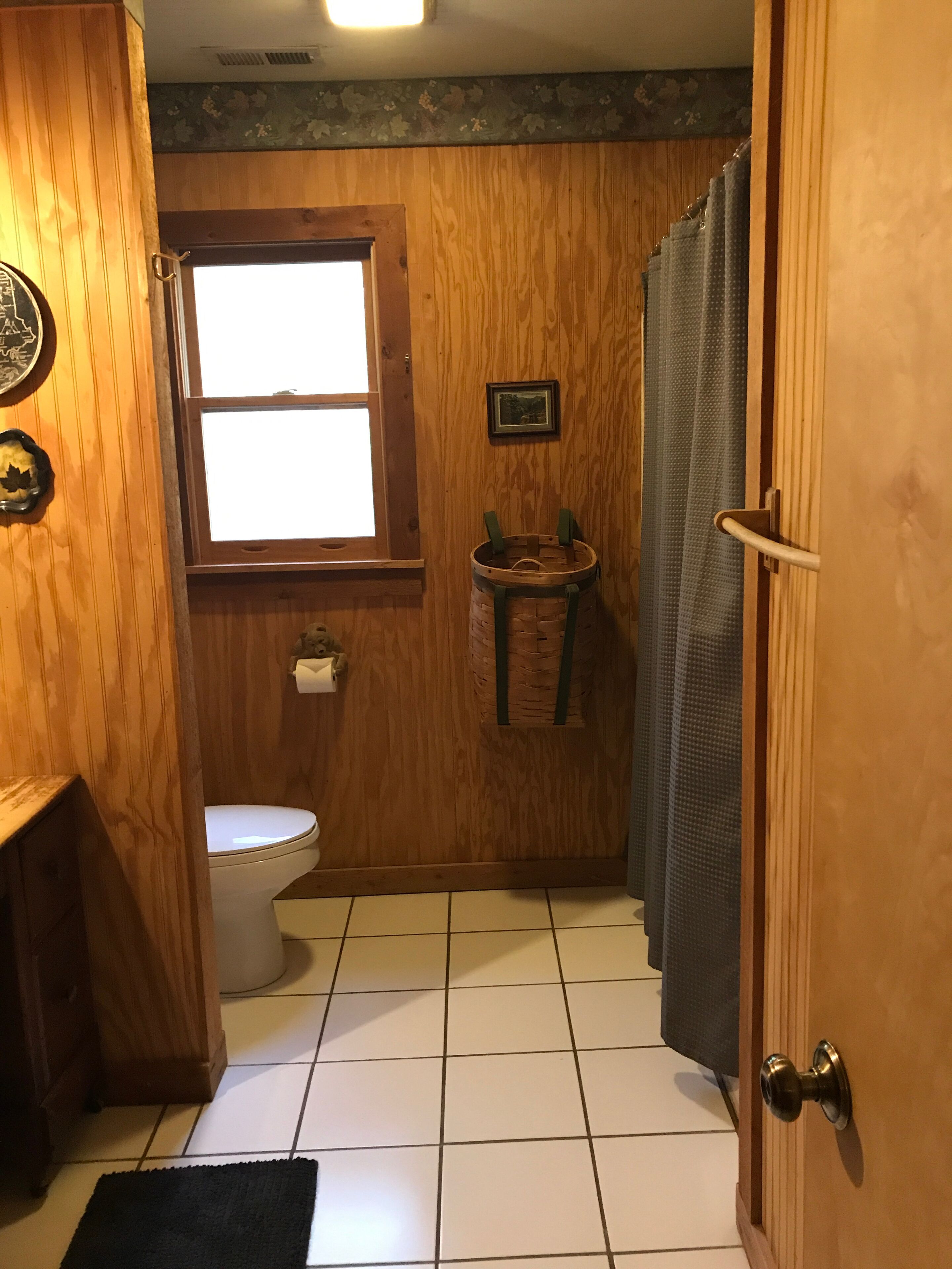 Une salle de bain en bois comprenant des toilettes, une fenêtre, un tableau encadré et un panier.
