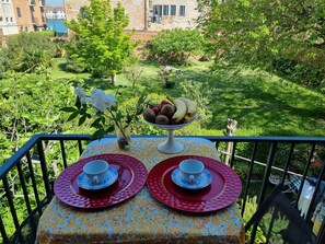 A table set with two cups and saucers, a bowl of fruit, and a vase with flowers, overlooking a lush garden and buildings. - RELAX GARDEN HOUSE WITH LAGOON VIEW (VENEZIA)