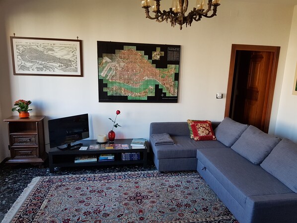 A living room with a sofa, a TV, a map, and a chandelier. - RELAX GARDEN HOUSE WITH LAGOON VIEW (VENEZIA)