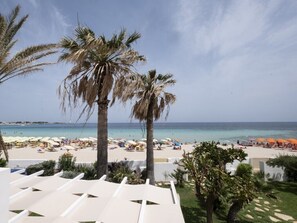 Vista de una playa con palmeras, zona de piscina y sombrillas.