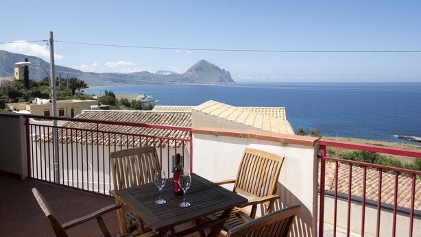 Ein Balkon mit Tisch, zwei Stühlen, einer Flasche und zwei Weingläsern.