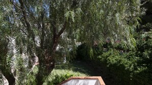 Ein Balkon mit weißer Brüstung und Blick auf einen üppigen Garten mit verschiedenen Bäumen und Sträuchern.