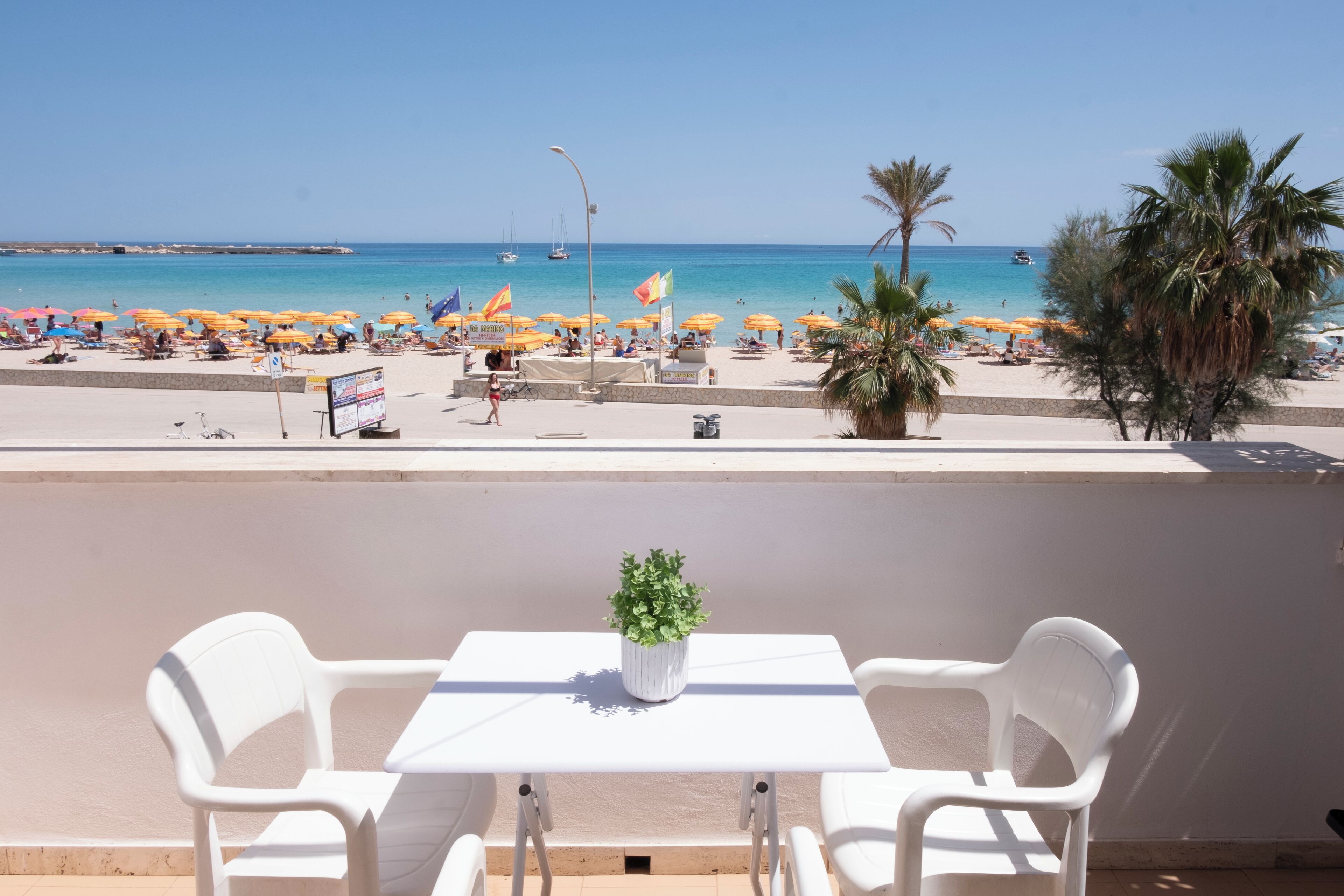 Ein Balkon mit Tisch und Stühlen, der auf einen Strand mit Sonnenschirmen und Menschen blickt.