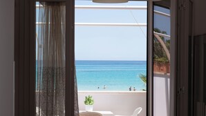 Quarto com vista para o mar, varanda com uma cadeira e uma planta, e um candeeiro de teto branco.