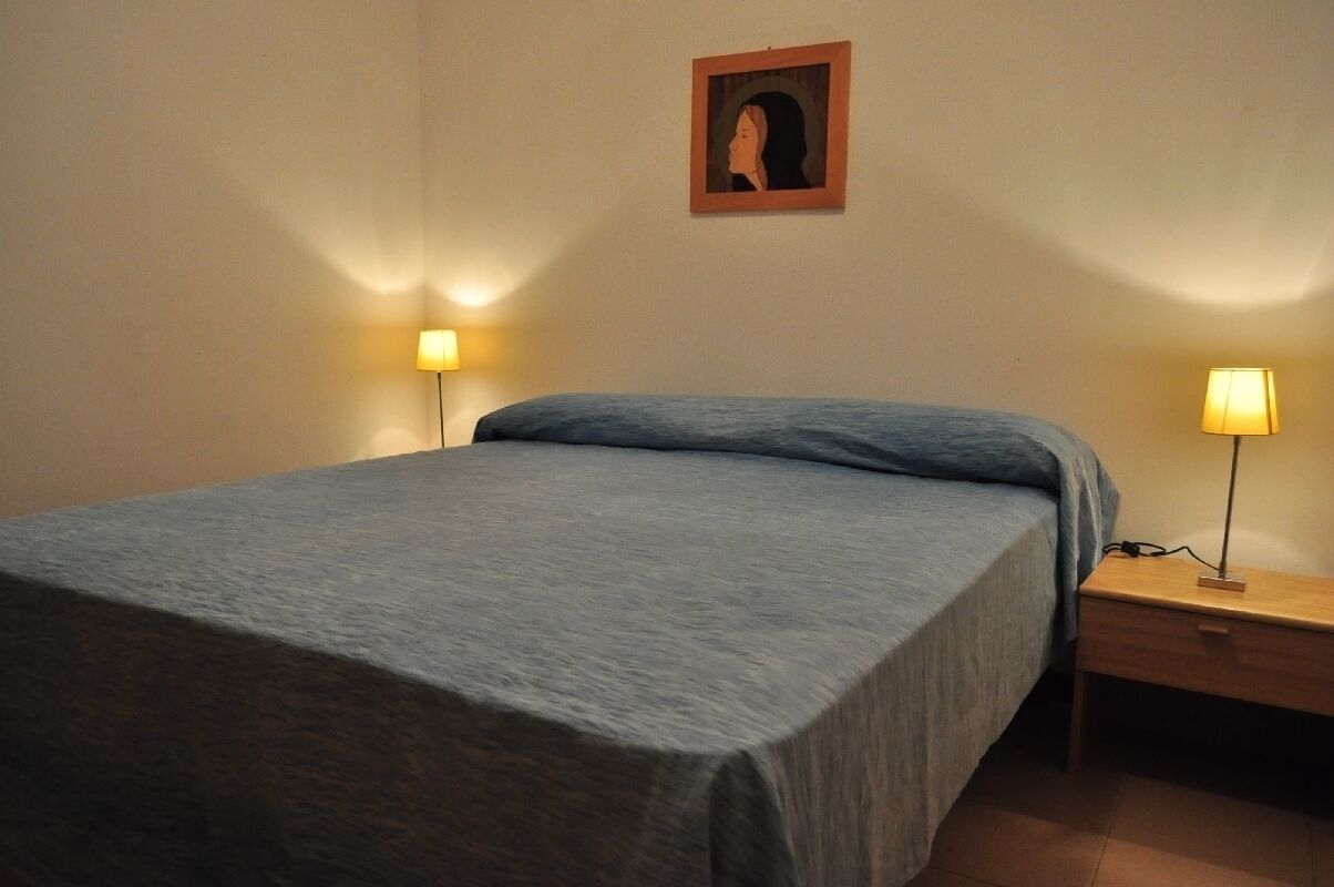 A neatly made bed with a blue bedspread and two bedside lamps on wooden nightstands.