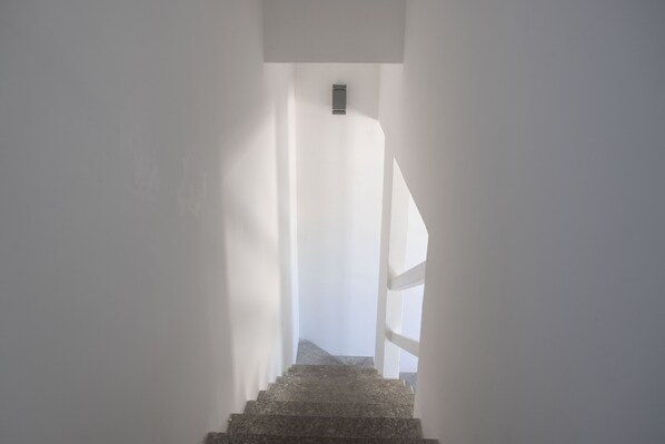 A narrow, white-walled stairway leading to a landing with a small, dark object on the wall. - Casa Blu sul mare e centralissima (San Vito Lo Capo)