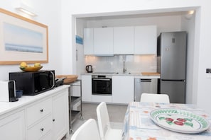 A compact kitchen with white cabinets, a microwave, a refrigerator, and a dining area with a table and chairs.