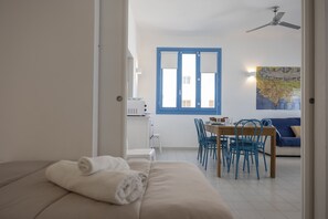 A room with a bed, a dining table with chairs, a ceiling fan, and a window with blue shutters.