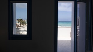 A room with two open doors leading to a balcony with a view of the beach and ocean.