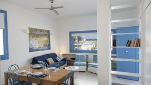 A dining area with a wooden table, blue chairs, and a ceiling fan. There is a sofa and a chair with a striped cover near a window.