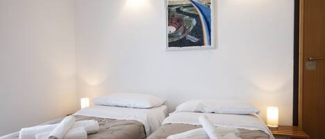 A hotel room with two beds, each with a beige quilt and white pillows, and a painting on the wall.