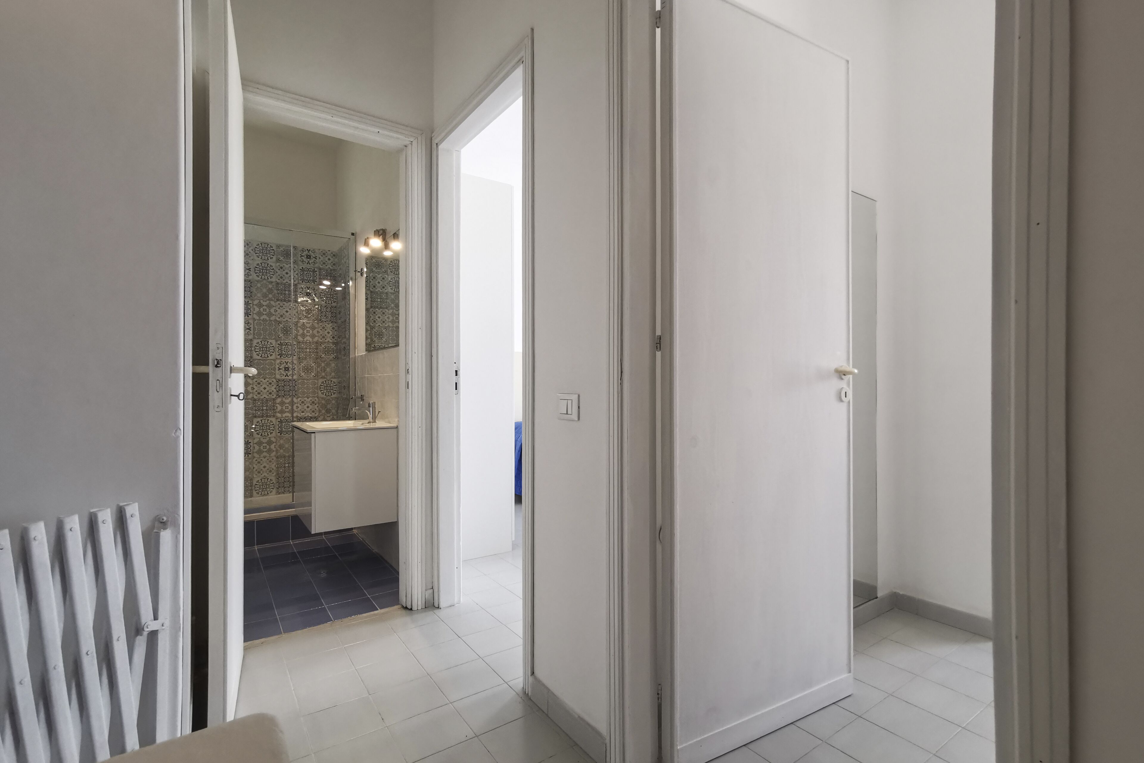 A hallway with white doors leading to a bathroom with a tiled shower and a sink.
