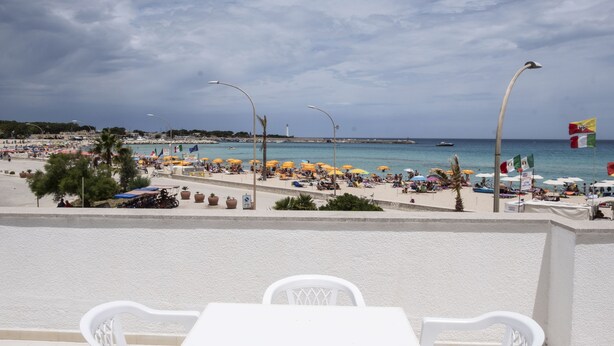A beachside view with a white table and chairs, umbrellas, and a flag.