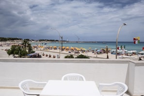 A beachside view with a white table and chairs, umbrellas, and a flag. - Casa Azzurra sul mare e centralissima (San Vito Lo Capo)