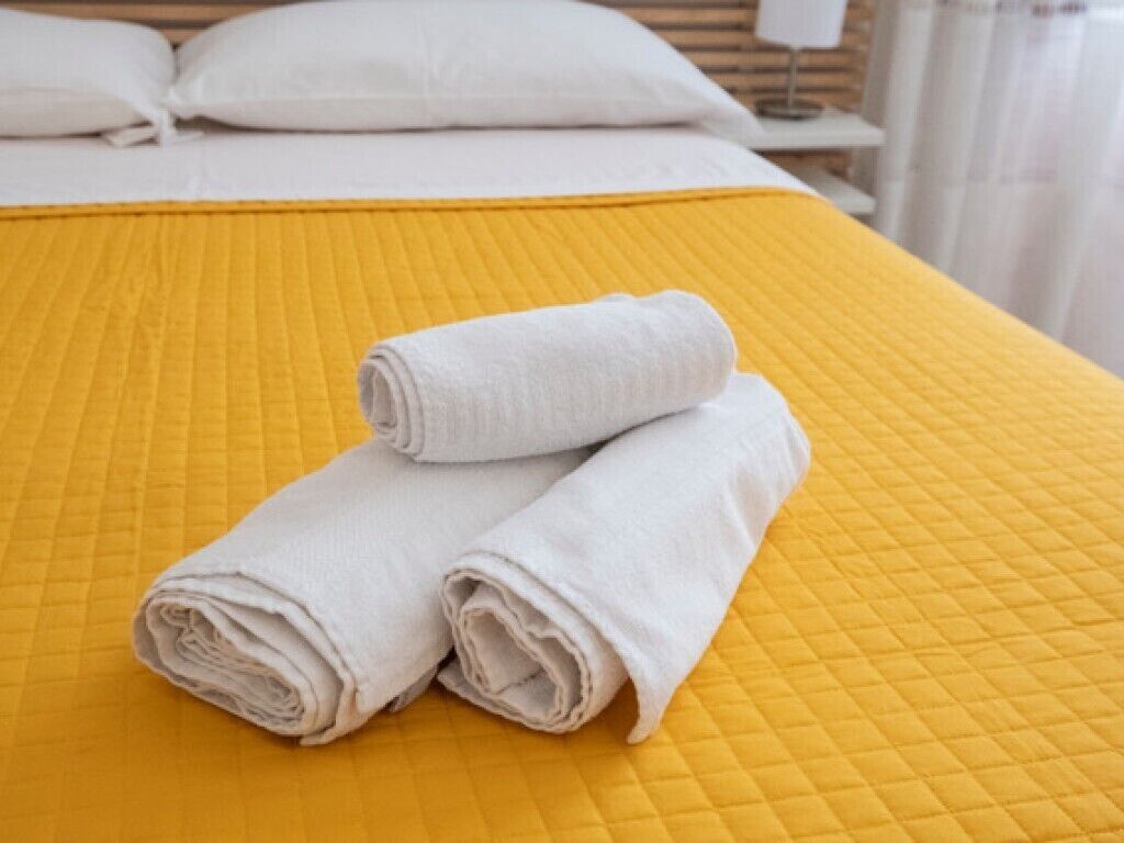 A bed with a yellow quilted bedspread and two neatly folded white towels.