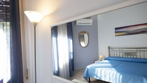 A bedroom with a bed, a mirror, and a painting on the wall. - Villa Faro (San Vito Lo Capo)