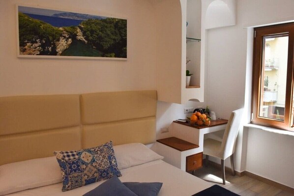 A bedroom with a bed, a desk, a chair, a window, and a painting on the wall.