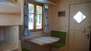A cabin interior with a wooden table, green bench, window with curtains, and a door with a window. - Schäferwagen am Berghof (Zeulenroda-Triebes)