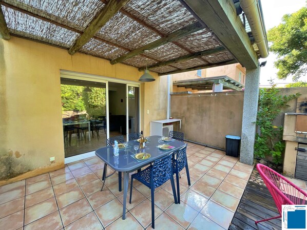 An outdoor patio with a table and chairs, a covered area with a thatched roof, and a sliding glass door leading to an indoor space.