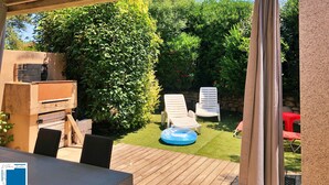Un patio in legno con un barbecue, due poltrone relax e una piccola piscina gonfiabile.