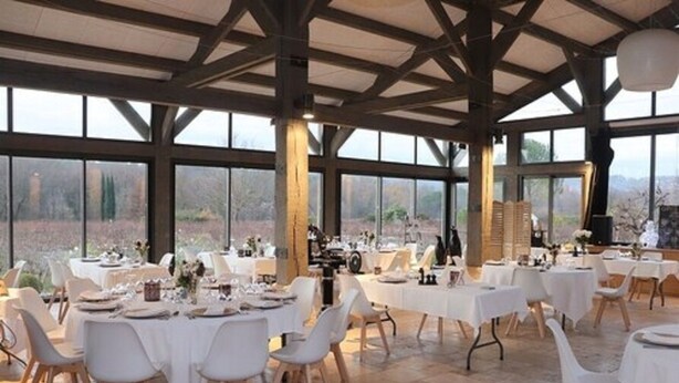 A spacious dining area with large windows, wooden beams, and white table settings.