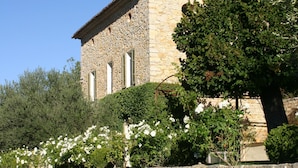 A stone building with a tiled roof, surrounded by greenery and white flowers.