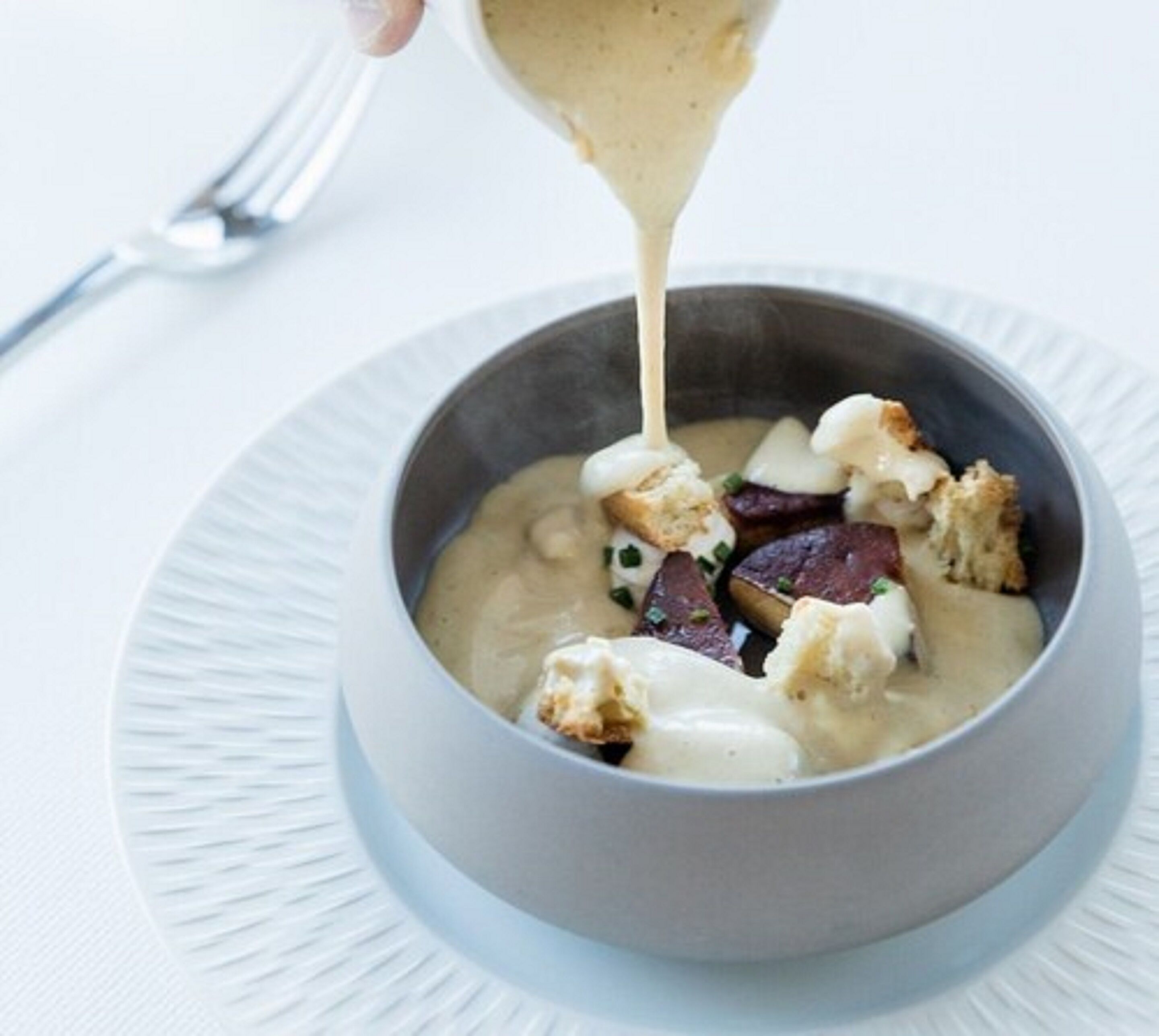 Un cuenco de sopa con croutons y verduras, mientras se vierte más.