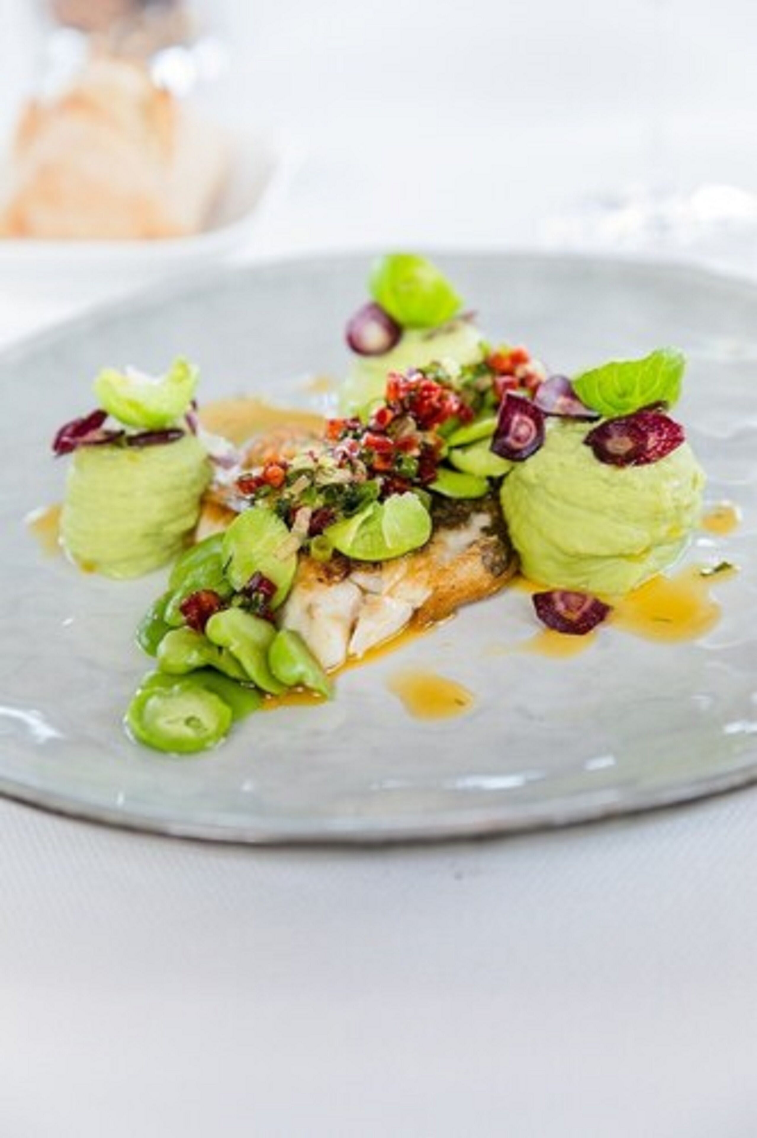 Een bord met visfilet, groene groenten en saus.