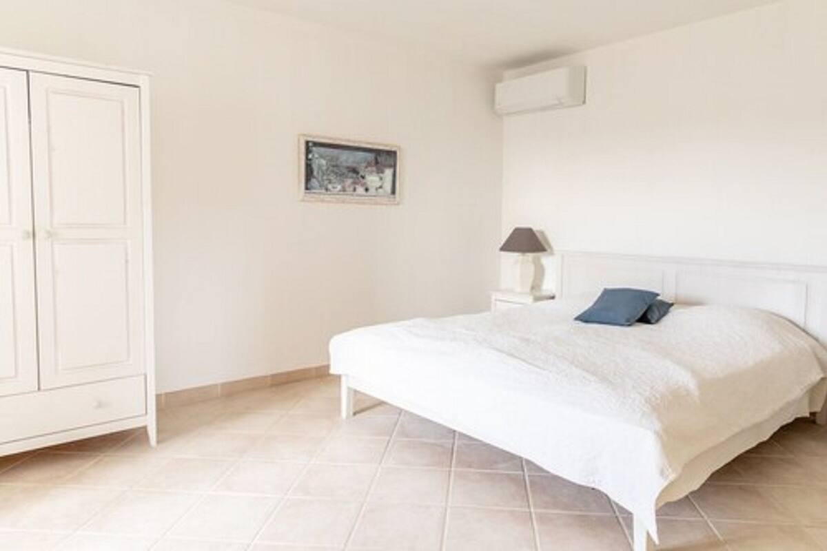 Een slaapkamer met een bed, nachtkastje, lamp, kledingkast en een lijst aan de muur.