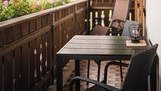 A wooden deck with a table and chairs, overlooking a garden with pink flowers and a distant building. - The Dorfblick vacation apartment with south-facing balcony two bedrooms, two bathrooms (Rodneck)