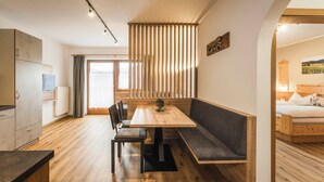 A modern, well-lit room with a wooden dining table, bench seating, and a view of a bedroom with a bed and a painting. - The Dorfblick vacation apartment with south-facing balcony two bedrooms, two bathrooms (Rodneck)