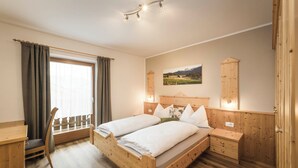 A wooden bedroom with a bed, bedside tables, a desk, and a chair. - The Dorfblick vacation apartment with south-facing balcony two bedrooms, two bathrooms (Rodneck)