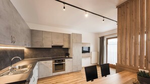 A modern kitchen with a wooden dining table, built-in appliances, and a large window. - The Dorfblick vacation apartment with south-facing balcony two bedrooms, two bathrooms (Rodneck)
