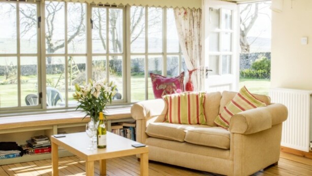 Ein gemütliches Wohnzimmer mit einem beigefarbenen Sofa, einem Holztisch und einem Blumenstrauß.