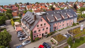 Et hotel med tagterrasse, parkeringsplads og udsigt over en sø og boligområde.