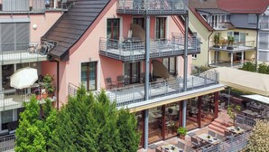 En bygning med flere etager, altaner, udendørs siddepladser og en overdækket terrasse.