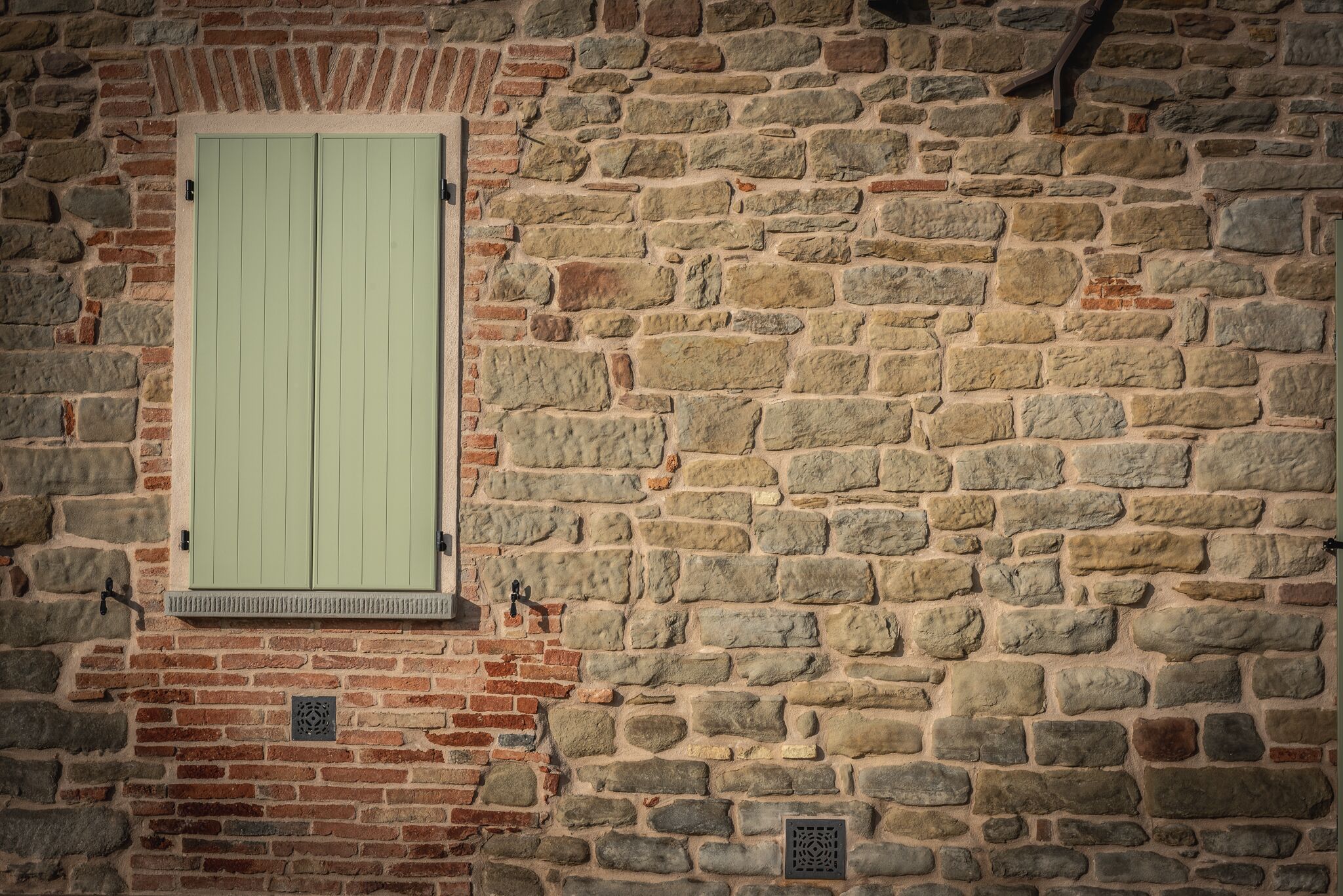 A stone wall with a green shutter window.