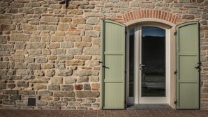 A stone wall with a door featuring green shutters. - Agriturismo Podere Ceriano (Modigliana)