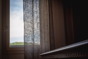 A window with sheer curtains, a view of greenery outside, and a portion of a wooden piece of furniture.