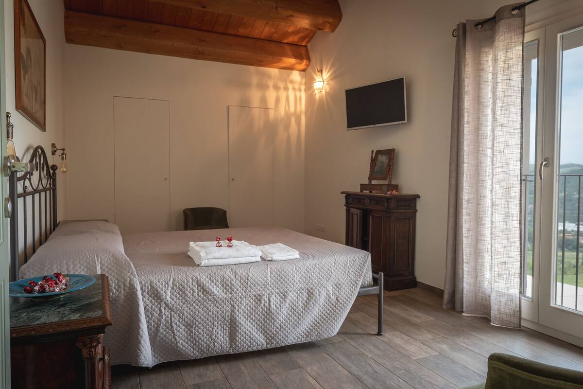 Une chambre à coucher avec un lit, un bureau sur lequel se trouve une assiette de nourriture, une chaise, une armoire, un téléviseur et une fenêtre avec des rideaux.