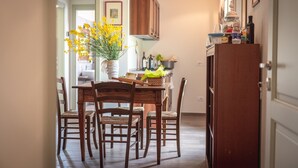 A dining area with a wooden table and chairs, a vase of yellow flowers, and a kitchen in the background. - Agriturismo Podere Ceriano (Modigliana)