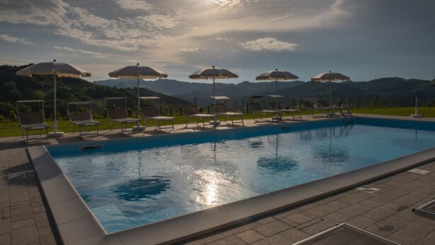 A swimming pool with sun umbrellas and lounge chairs, surrounded by a landscaped area with hills in the background. - Agriturismo Podere Ceriano (Modigliana)