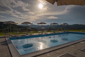 A swimming pool with sun umbrellas and lounge chairs, surrounded by a landscaped area with hills in the background.