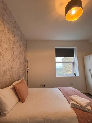 A bedroom with a bed, a window, a wall-mounted light fixture, and a wardrobe. - 30 Beckenham Studios (Beckenham)