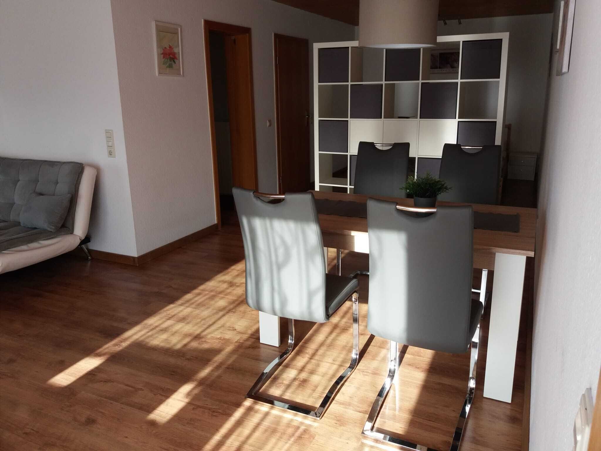 Una sala de estar moderna con un sofá gris, una mesa de comedor de madera con cuatro sillas y una estantería empotrada.